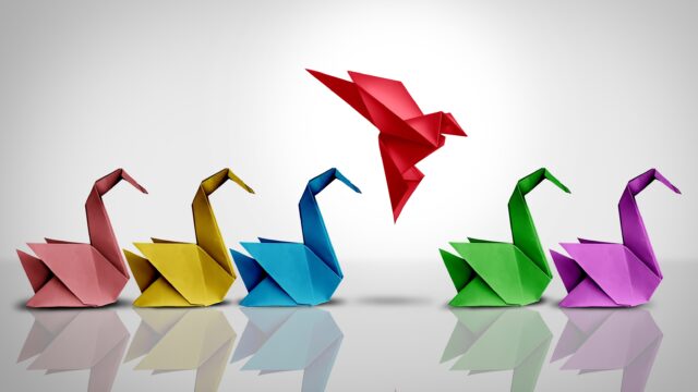 Innovative thinker concept and new idea thinking as a symbol of revolutionary innovation and inspiration metaphor as a group of paper swans and a game changer origami bird in flight.